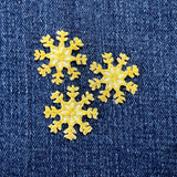 Three small, embroidered, yellow-gold snowflake patches are shown resting on a  denim fabric.