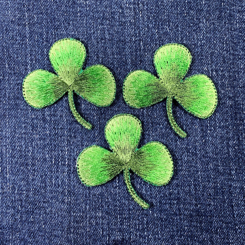 Three green embroidered shamrock patches on denim fabric