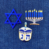 Embroidered patches of a Star of David, a menorah with lit candles, and a dreidel on denim fabric.