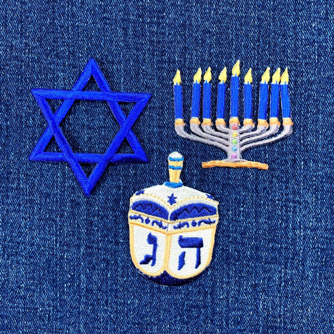 Embroidered patches of a Star of David, a menorah with lit candles, and a dreidel on denim fabric.