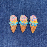 Three glittery ice cream cone patches on a denim background