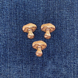 Three embroidered patches depicting the image of a mushroom with a brown cap and white stem, arranged on a denim background