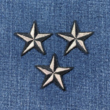 Three silver and black star-shaped patches on a denim background