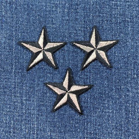 Three silver and black star-shaped patches on a denim background