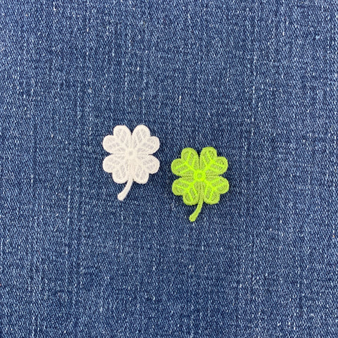 a green and a white 4 leaf clover patch on a denim background