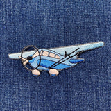 A blue and gray embroidered airplane patch with an iron on backing, displayed on a denim background