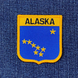 Alaska state patch with blue background and yellow border on denim fabric