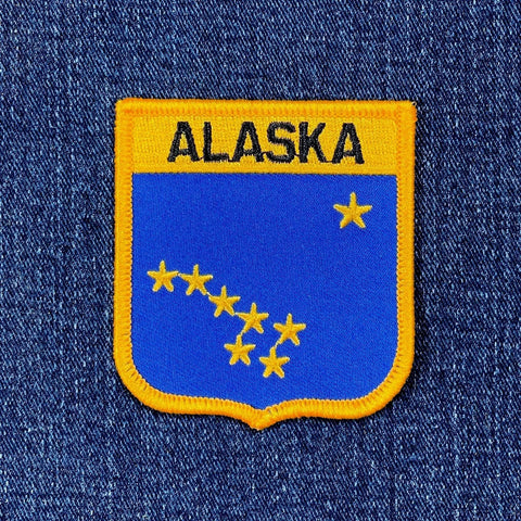 Alaska state patch with blue background and yellow border on denim fabric