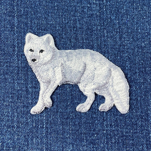Embroidered patch of an arctic fox in white and grey colors on a denim background