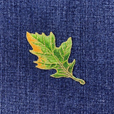 A green oak leaf applique patch with an iron-on backing on a denim background