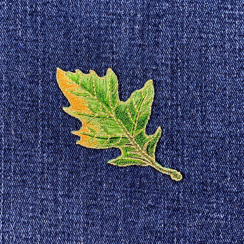 A green oak leaf applique patch with an iron-on backing on a denim background