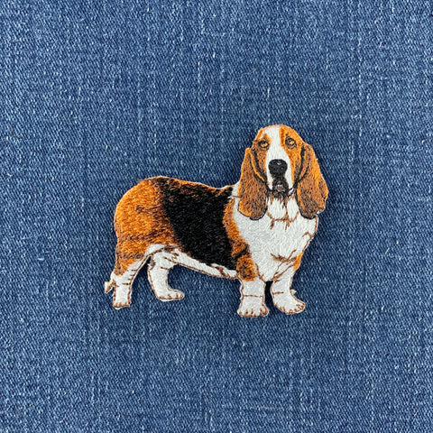 An embroidered basset hound patch in brown, white, and black, placed on a blue denim fabric background.