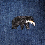 A black bear applique patch with a salmon fish embroidered on its mouth on a denim background