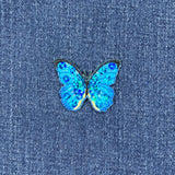 A blue butterfly applique patch with mini sequin shimmery embroidery on a denim background