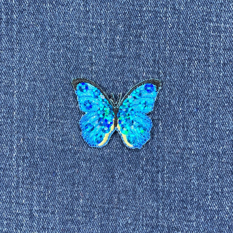 A blue butterfly applique patch with mini sequin shimmery embroidery on a denim background