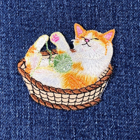 Embroidered patch of a cat inside a basket on a denim background