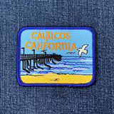 Cayucos California embroidered patch featuring a beach, pier, and seagull on a denim background.