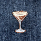 an embroidered patch of a chocolate espresso martini on a denim background