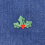 Embroidered green holly leaves with red berries patch, designed as a Christmas decoration displayed on a denim background