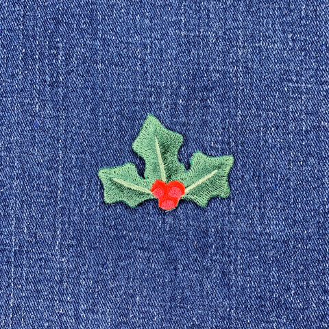 Embroidered green holly leaves with red berries patch, designed as a Christmas decoration displayed on a denim background