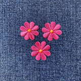Three pink flower-shaped patches on a denim background
