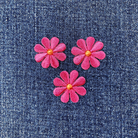 Three pink flower-shaped patches on a denim background