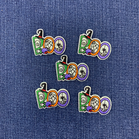 Five Halloween-themed embroidered patches spelling 'BOO' in green, orange, purple, and white, arranged on a blue denim fabric background.