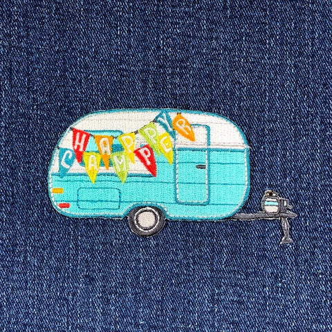 applique patch depicting a blue camper RV with the text 'HAPPY CAMPER' in multi-colored letters hanging from the front, displayed on a denim background