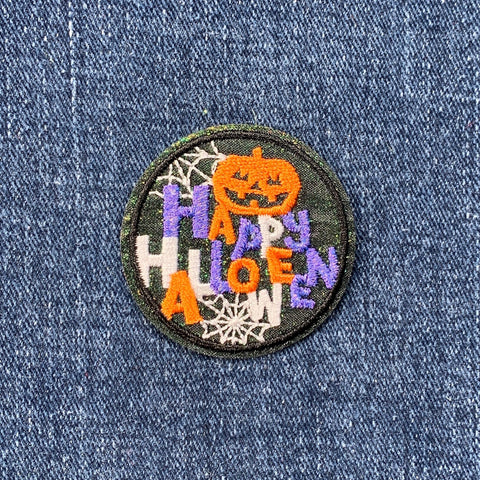 Halloween-themed patch with a pumpkin and spider webs on denim fabric.