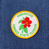 Embroidered patch of the Hawaii state flower, hibiscus, on a denim background.