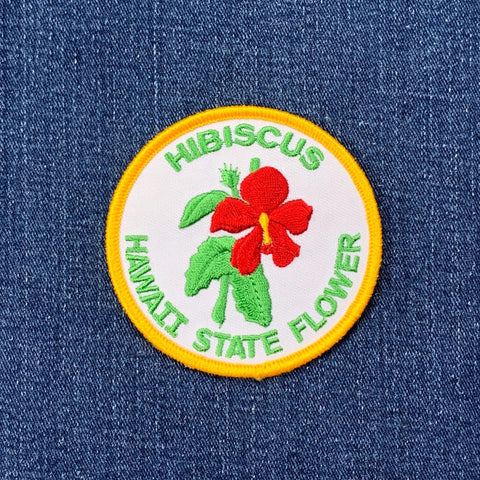 Embroidered patch of the Hawaii state flower, hibiscus, on a denim background.