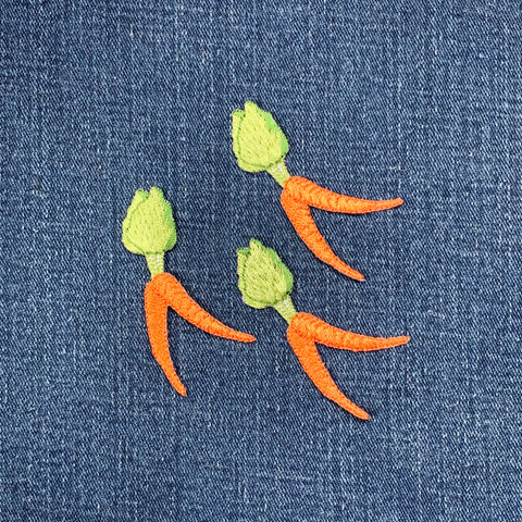 three small, embroidered carrot applique patches on a denim background