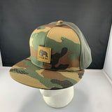 Camouflage baseball cap with a LET'S BE IRIE logo patch on a mannequin head against a black background