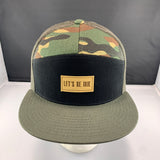 Camouflage trucker hat with a black front panel, an olive bill, and 'Let's Be Irie' patch on a black background