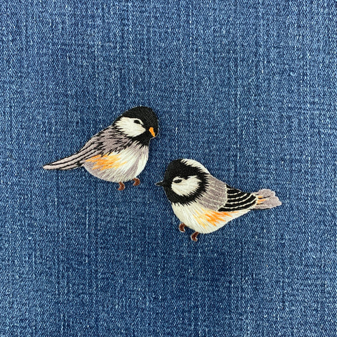 Two embroidered bird patches on a denim background