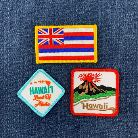 Three embroidered patches on a denim background, featuring the Hawaiian flag, 'Hawaii Land of Aloha', and a volcano design.
