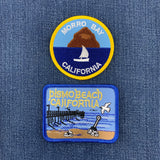 Two embroidered patches on a blue denim background, featuring Morro Bay and Pismo Beach, California.