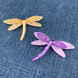 Two dragonfly-shaped patches, one gold and one purple, on a denim background.