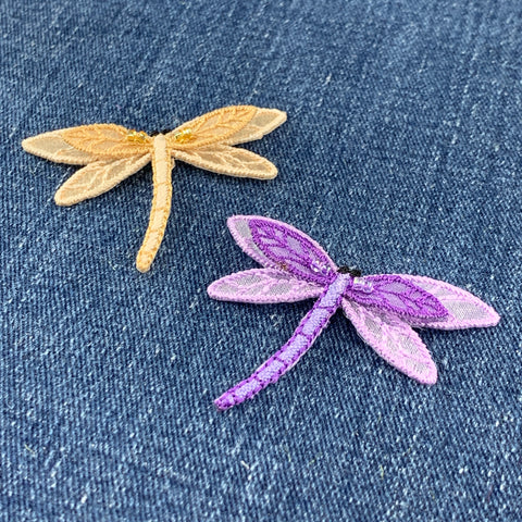 Two dragonfly-shaped patches, one gold and one purple, on a denim background.