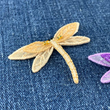 Two embroidered dragonfly patches, one gold and one purple, on a denim background.