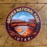 A circular vinyl decal featuring the Arches National Park logo with a stylized depiction of a desert landscape and a blue sky.