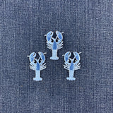 Three lobster-shaped patches in light blue, arranged on a textured blue denim fabric background.
