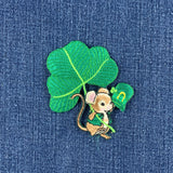 A small embroidered St. Patrick's Day mouse patch featuring a brown mouse in a green hat and outfit under a large green shamrock leaf, shown on a blue denim background.
