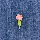 A small embroidered pink flower patch with green leaves on a blue denim fabric background.
