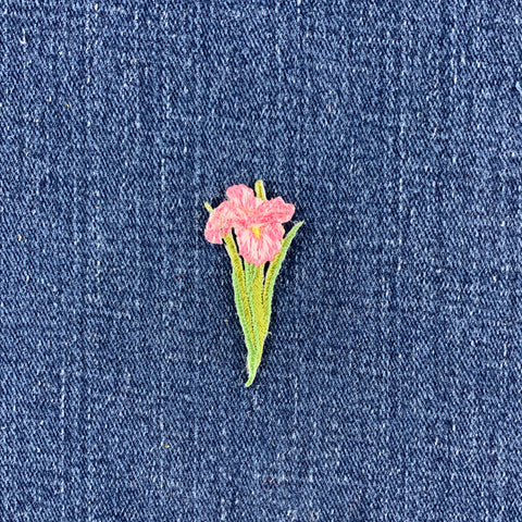 A small embroidered pink flower patch with green leaves on a blue denim fabric background.