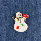 A snowman patch with a red 'HOPE' sign, placed on a blue denim background.