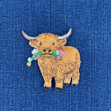 a highland cow embroidered patch displayed on a denim background