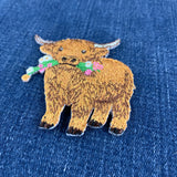 a highland cow embroidered patch displayed on a denim background