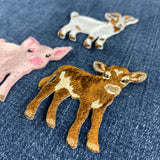 Three embroidered animal patches shaped like a pig, a white goat, and a brown calf, displayed on a blue denim fabric background.