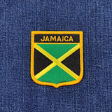 A shield-shaped embroidered patch with the text 'JAMAICA' and the colors of the Jamaican flag on a denim background